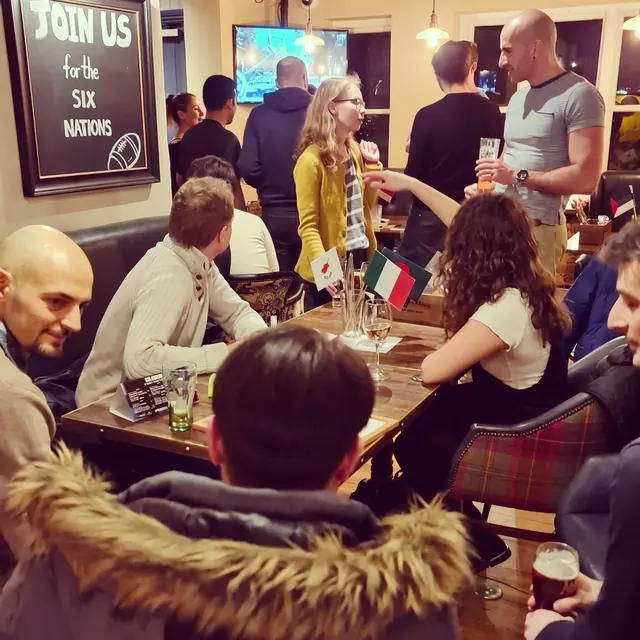 People chatting across tables with flags at a busy Guildford Babel evening